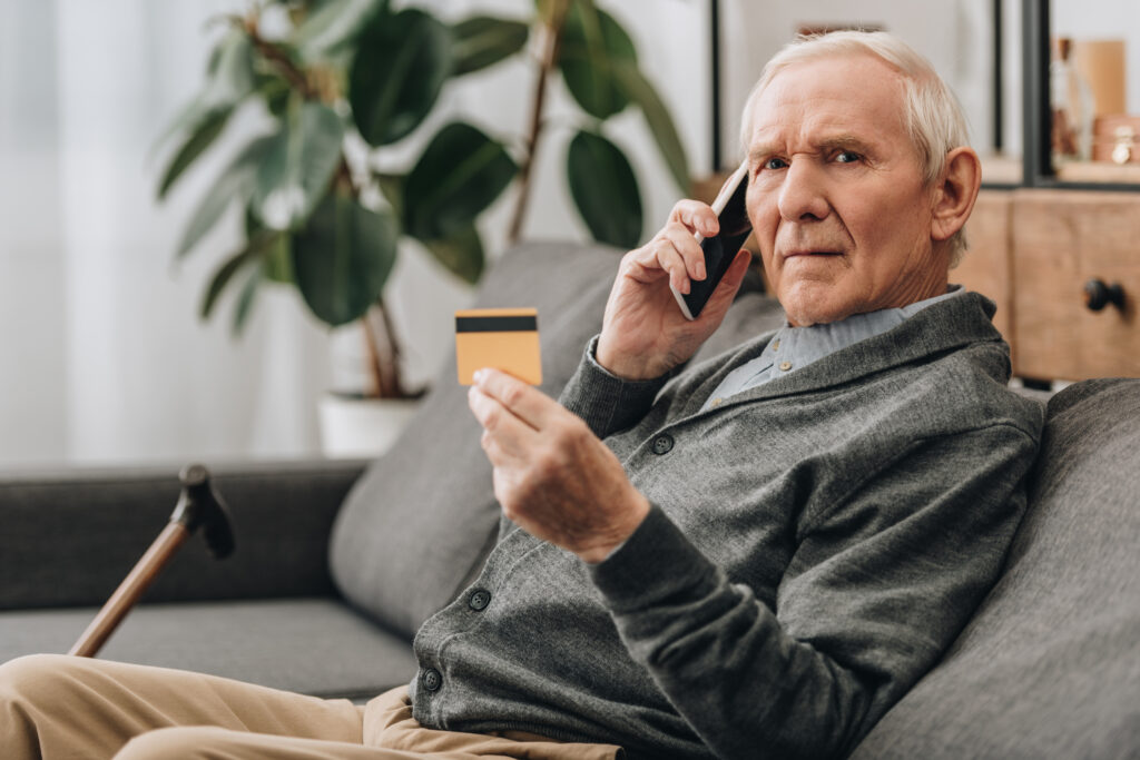 senior man talking on smartphone and holding credit card